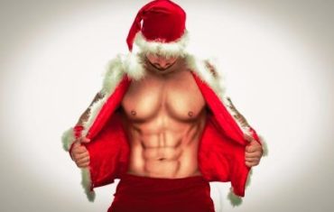 Mladý svalnatý muž s Santa klobúkom demonštruje svoje svaly.