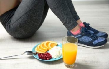 Žena drží zónovú diétu, sedí a podlahe a vedľa seba má zdravé raňajky