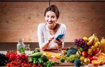 Usmiata žena drží zdravú diétu a má pred sebou na stole ovocie, zeleninu a vodu
